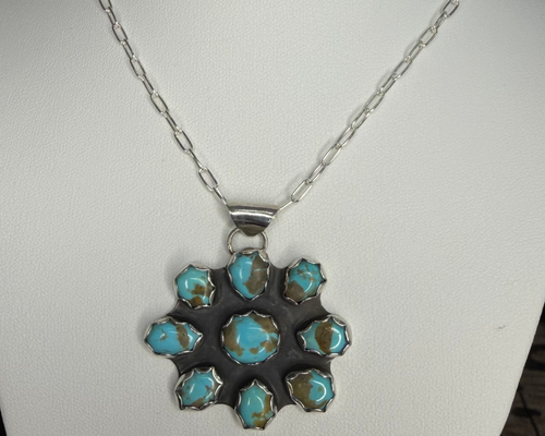 A silver chain necklace with a floral cluster pendant featuring turquoise-blue and brown stones, displayed on a white mannequin bust.